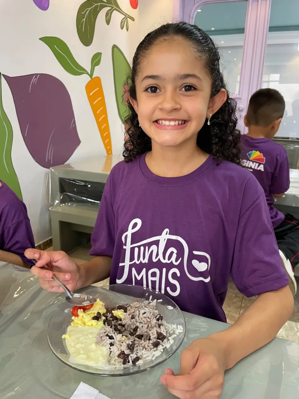 Criança da Junta Mais sorrindo diante de um prato de arroz, feijão e ovos durante a refeição, em Curitiba