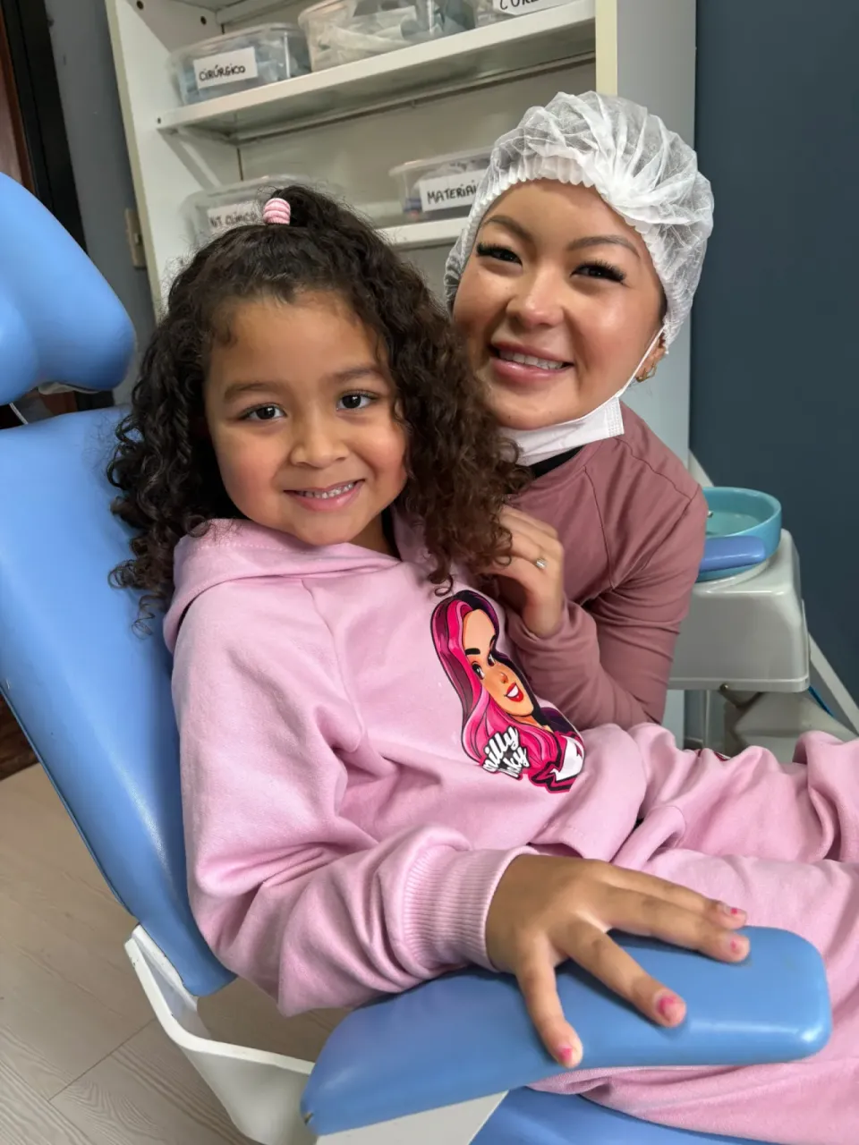 Dentista voluntária e criança sorrindo na cadeira do consultório odontológico da Junta Mais, em Curitiba