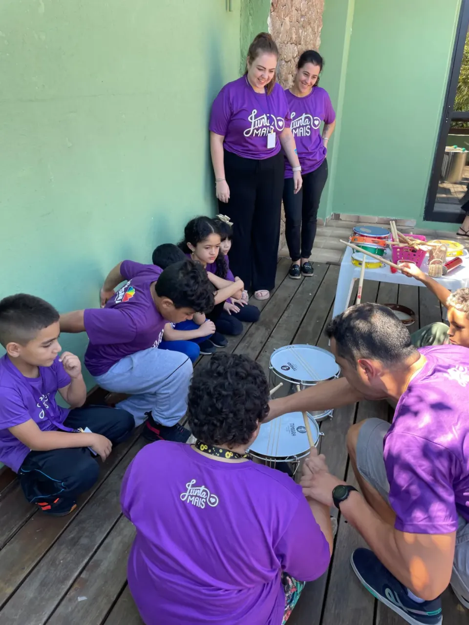 Crianças da Junta Mais em oficina de percussão com instrutor, ao ar livre, em Curitiba