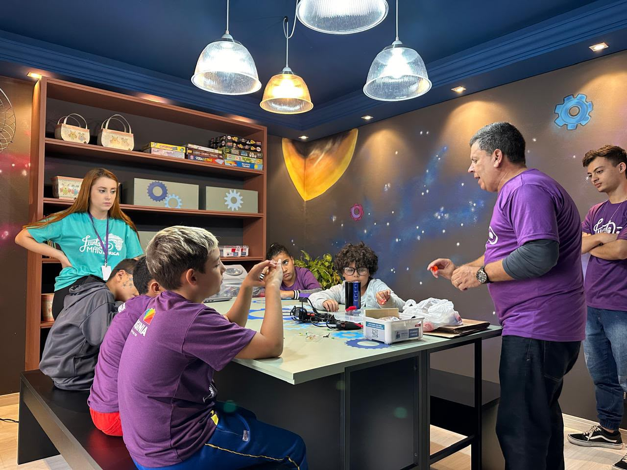 Crianças e educador da Junta Mais em oficina de robótica sustentável, em sala temática, em Curitiba