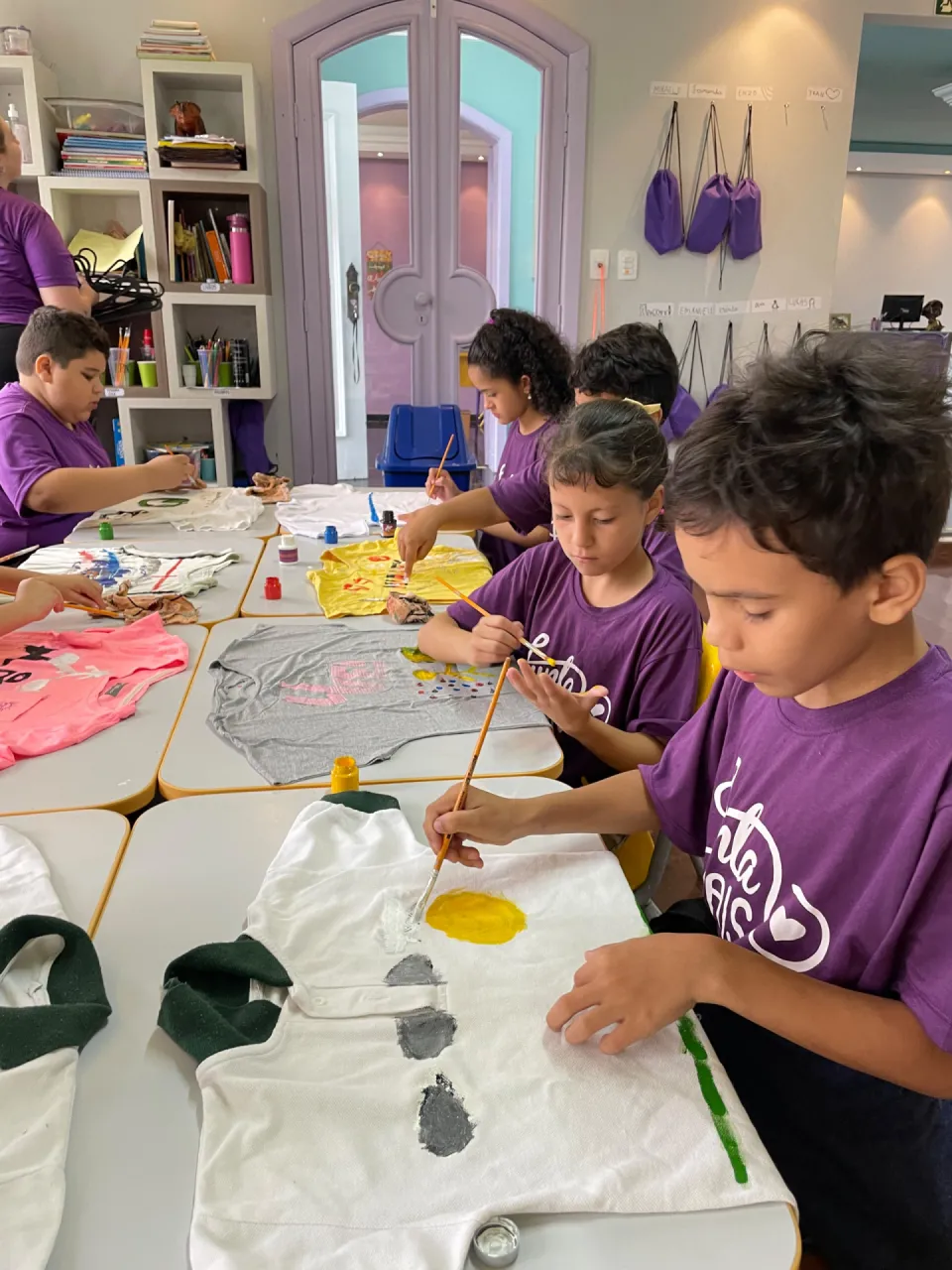 Crianças da Junta Mais pintando peças de tecido em oficina de arte, em Curitiba