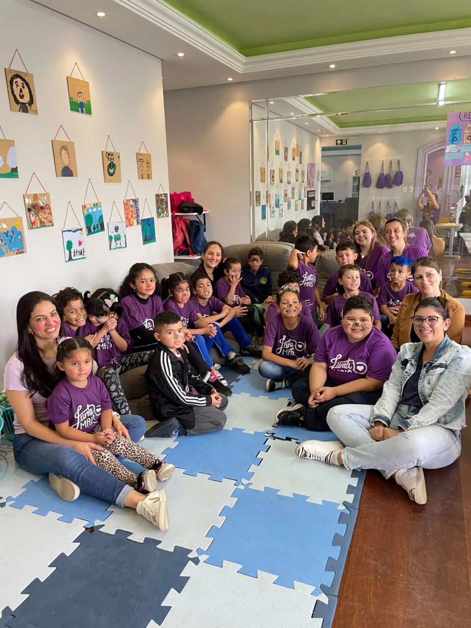 Grande grupo de crianças com pintura facial e educadoras da Junta Mais reunidos na sede, em Curitiba